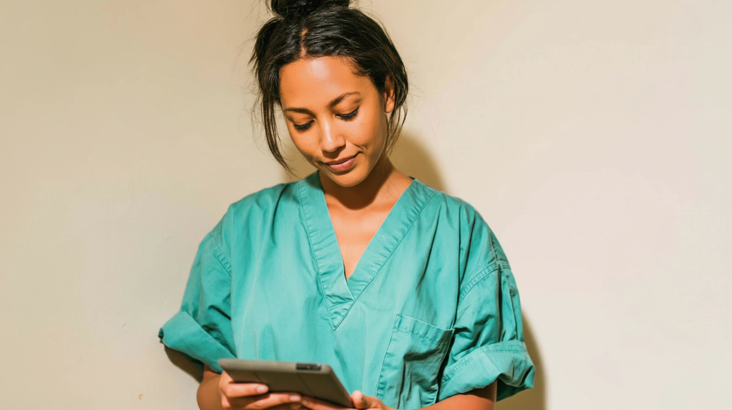 A nurse in teal scrubs reading from a tablet held in both hands