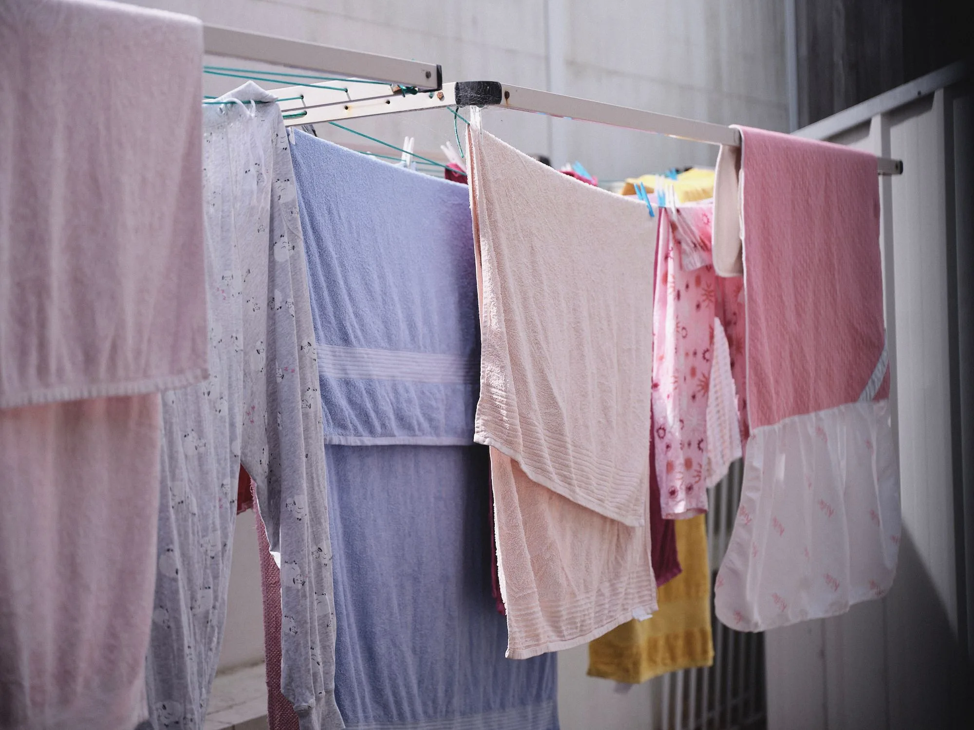 Towels, pyjamas and a pink blanket drying on an outdoor clothes airer beside a pale wall